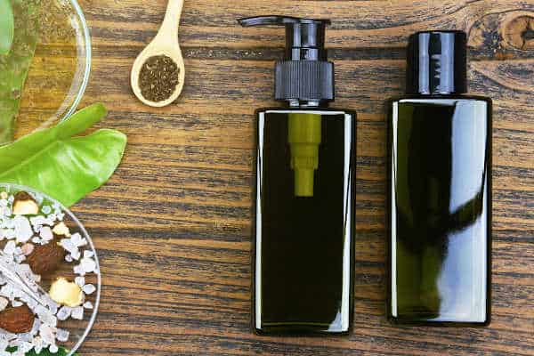 green skincare product bottles next to a spoon and plants