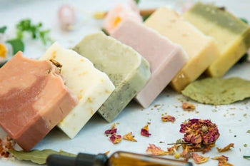 natural bars of soap in a variety of colors laying at an angle next to dried botanicals