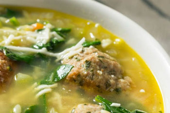 bowl of soup with broth, spinach, carrots, meatballs, parmesan cheese