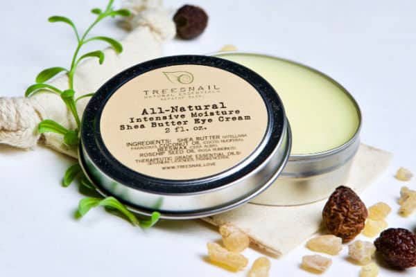 jar of shea butter eye cream next to rose hips and frankincense resin on a cotton bag