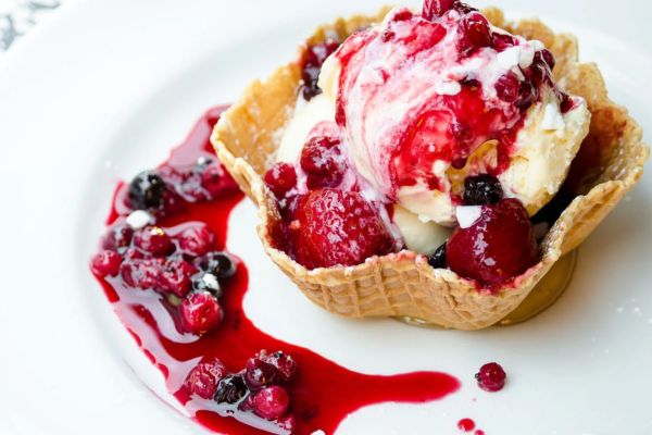 vanilla ice cream in a waffle cone bowl covered with red and blue berries and sauce