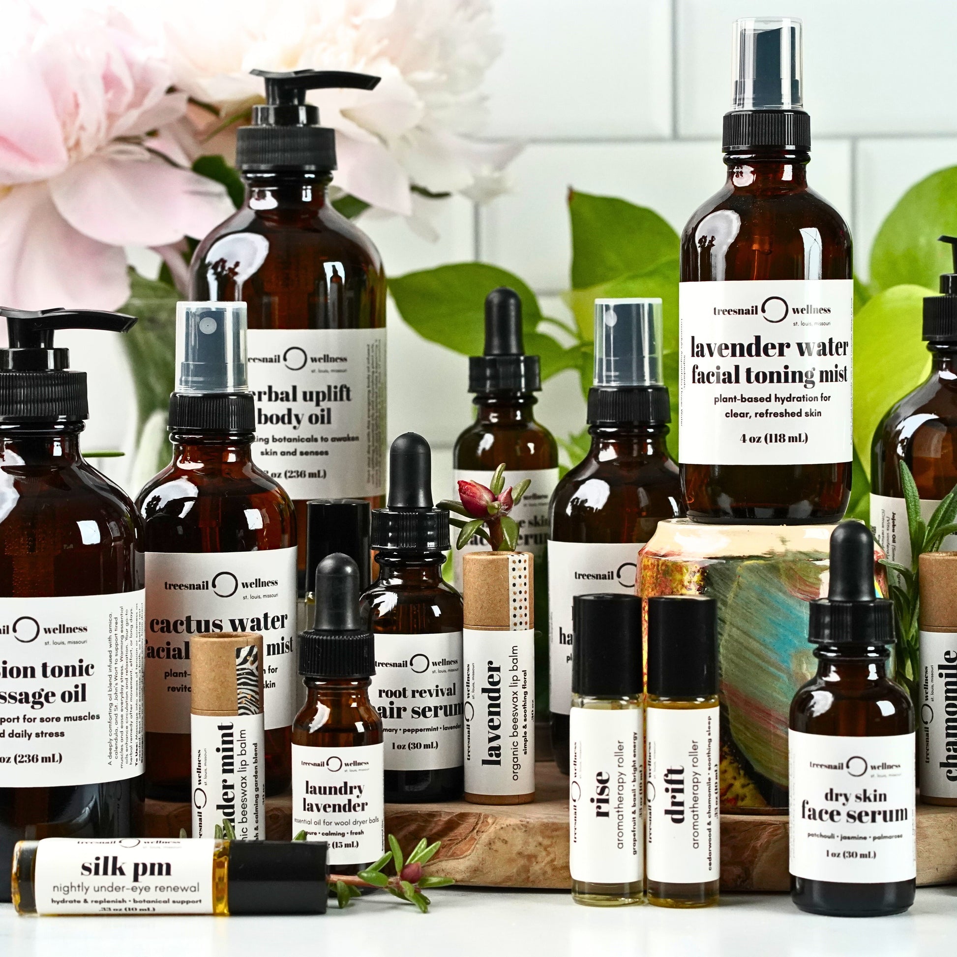 Collection of various skincare and wellness products on a white surface with greenery in the background.