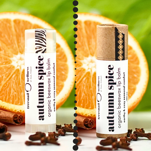 Two lip balms labeled 'autumn spice' with oranges and cinnamon sticks in the background by Treesnail Wellness.