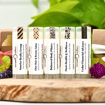 Set of organic lip balms with various business labels on a wooden surface with greenery in the background