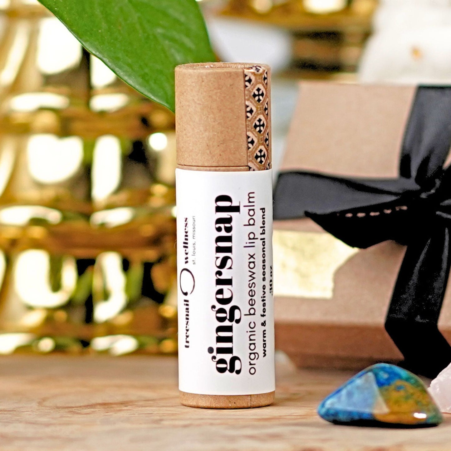 Gingersnap organic beeswax lip balm on a wooden surface with a blurred background by Treesnail Wellness