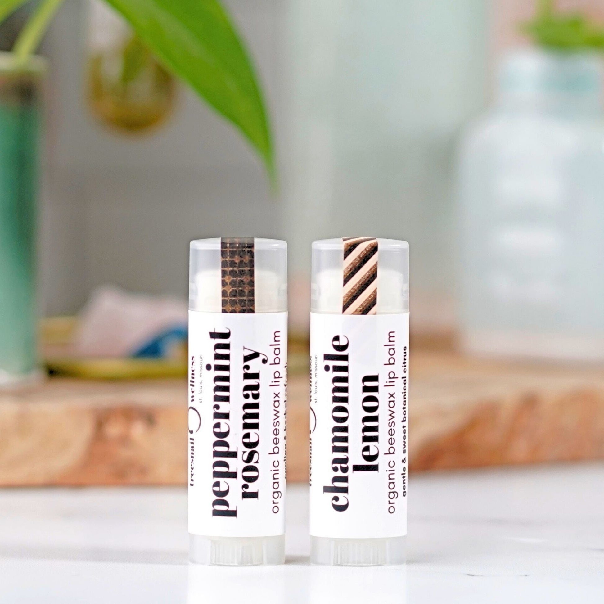 Two organic beeswax lip balm tubes on a white surface with a blurred natural background.