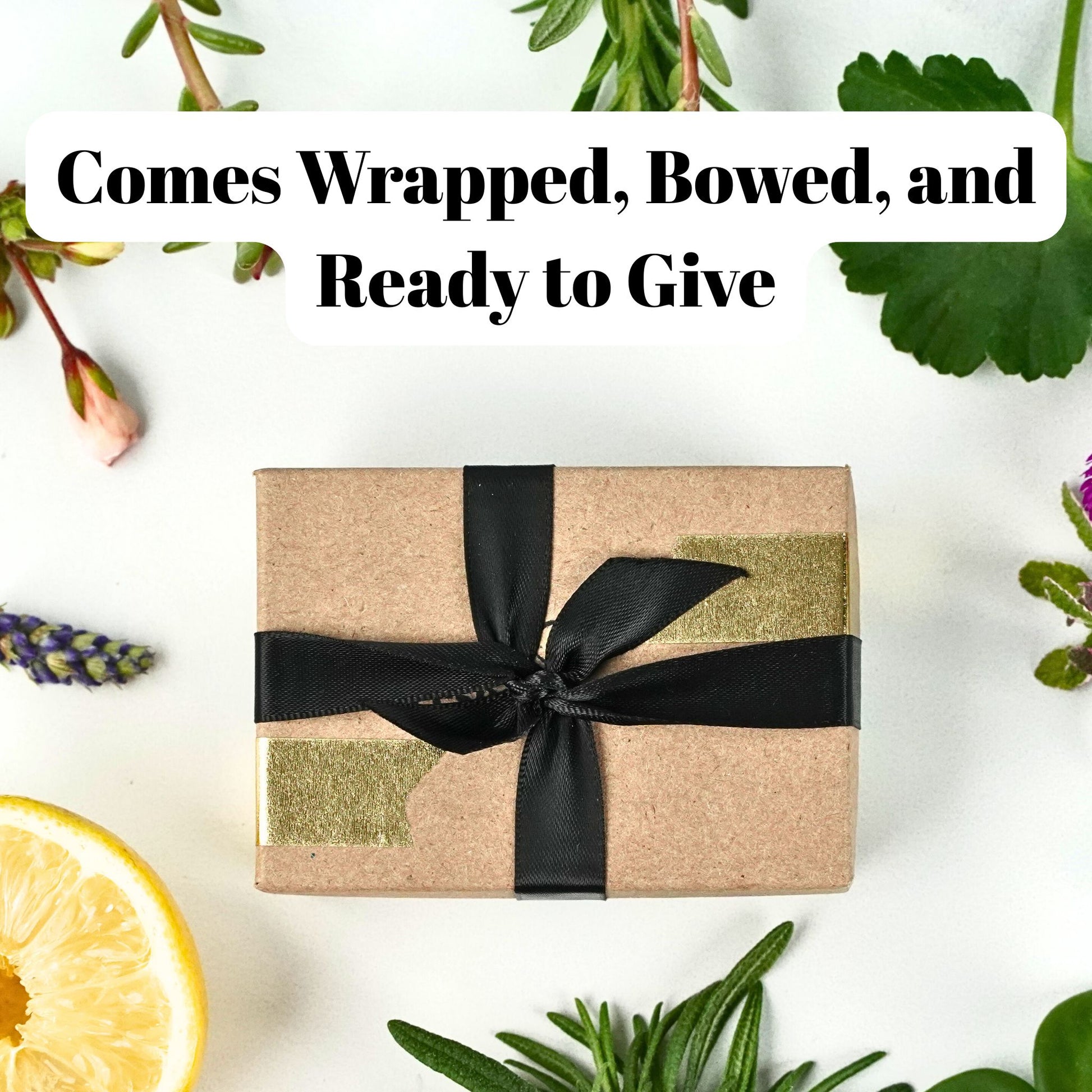 Gift box wrapped in brown paper with a black ribbon, surrounded by greenery and a slice of lemon.