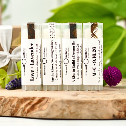 Set of wedding favor lip balms with personalized text on a wooden surface with greenery in the background